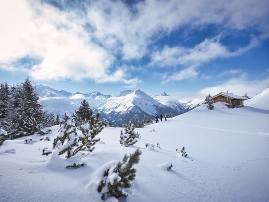 Das Maiensee: Ihr Hotel in St. Christoph Verschneite Berglandschaft mit Tannen und einer kleinen Holzhütte bei klarem Himmel