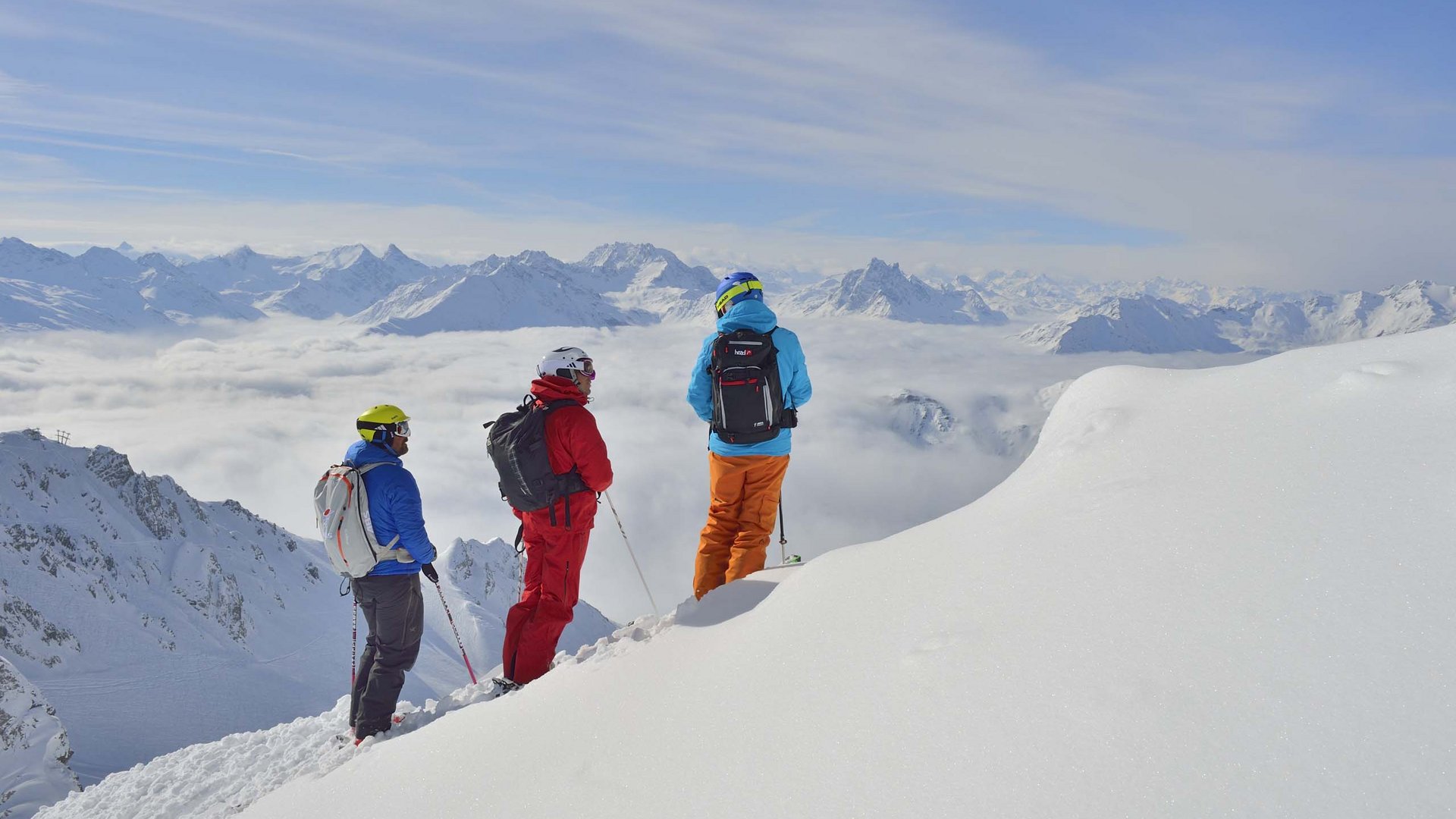 Hotel Maiensee: Wintersport am Arlberg Drei Skifahrer schauen von verschneitem Berggipfel auf Wolken und Alpen