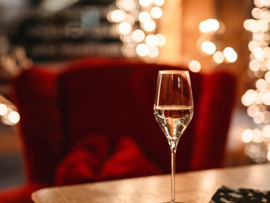 Die Lounge-Bar in Ihrem Skihotel am Arlberg Weinglas mit Weißwein auf einem Holztisch in gemütlicher Umgebung
