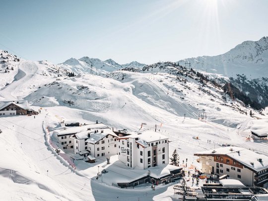 Die Lounge-Bar in Ihrem Skihotel am Arlberg Schneebedeckte Berglandschaft mit Hotels und Skifahrern an sonnigem Wintertag