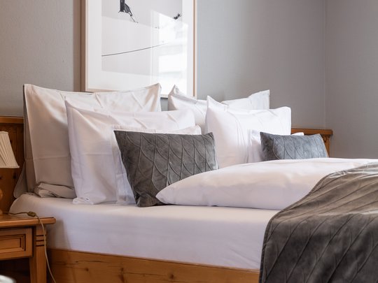Das Maiensee: Ihr Hotel in St. Christoph Gemütliches Doppelbett mit vielen Kissen und grauer Decke in einem hellen Zimmer