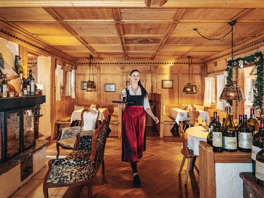 Ihr Hotel in St. Christoph am Arlberg Kellnerin in traditioneller Kleidung serviert Wein in gemütlichem Holzrestaurant