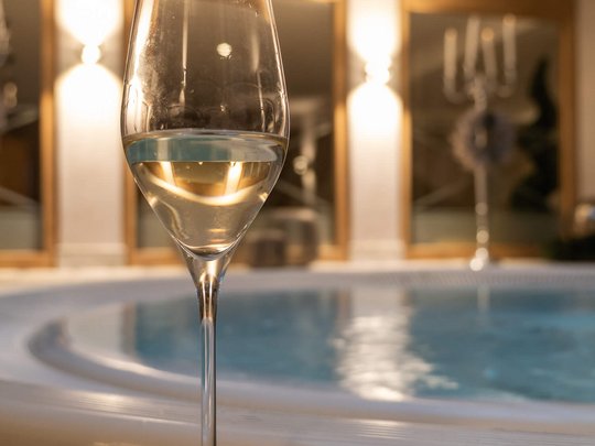 Maiensee: Ihr Wellnesshotel bei St. Anton Weißweinglas vor einem Whirlpool in einem warm beleuchteten Raum