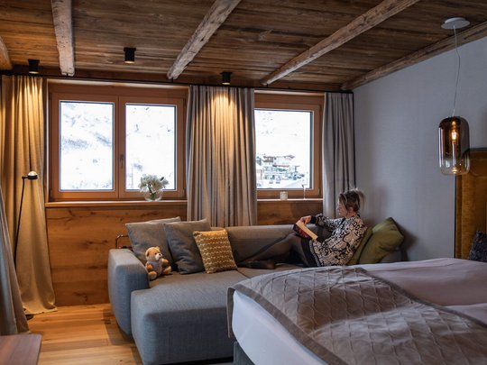 Das Maiensee: Ihr Hotel in St. Christoph Frau liest auf Sofa im gemütlichen Zimmer mit Holzbalkendecke und Alpenblick