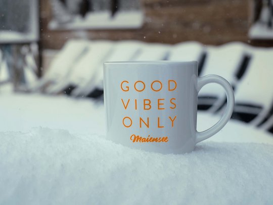 Burger im Skihotel in St. Anton am Arlberg Tasse mit Aufschrift Good vibes only im Schnee vor einer Bank
