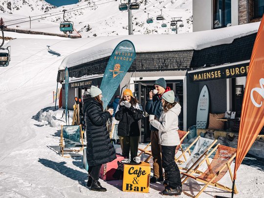 Burger im Skihotel in St. Anton am Arlberg Gruppe trinkt Kaffee vor Bergcafé im Schnee mit Sessellift im Hintergrund