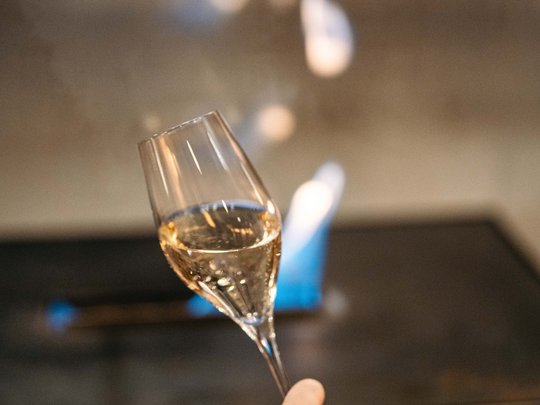 Die Lounge-Bar in Ihrem Skihotel am Arlberg Hand hält ein Weinglas mit weißem Wein vor unscharfem Hintergrund