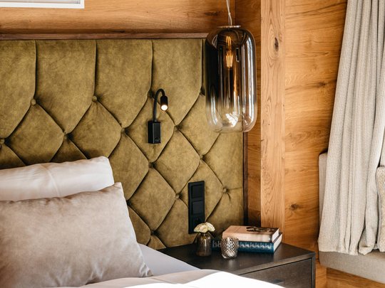 Das Maiensee: Ihr Hotel in St. Christoph Gemütliches Schlafzimmer mit grünem gepolstertem Kopfteil und Holzwänden.