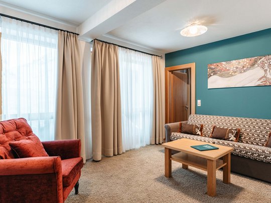 Das Maiensee: Ihr Hotel in St. Christoph Gemütliches Wohnzimmer mit rotem Sessel, Sofa, Holzttisch und Kunst an der Wand