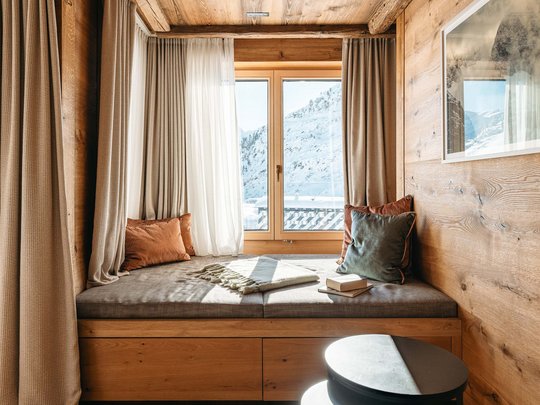 Das Maiensee: Ihr Hotel in St. Christoph Gemütliche Sitzecke am Fenster mit Kissen und Blick auf verschneite Berge