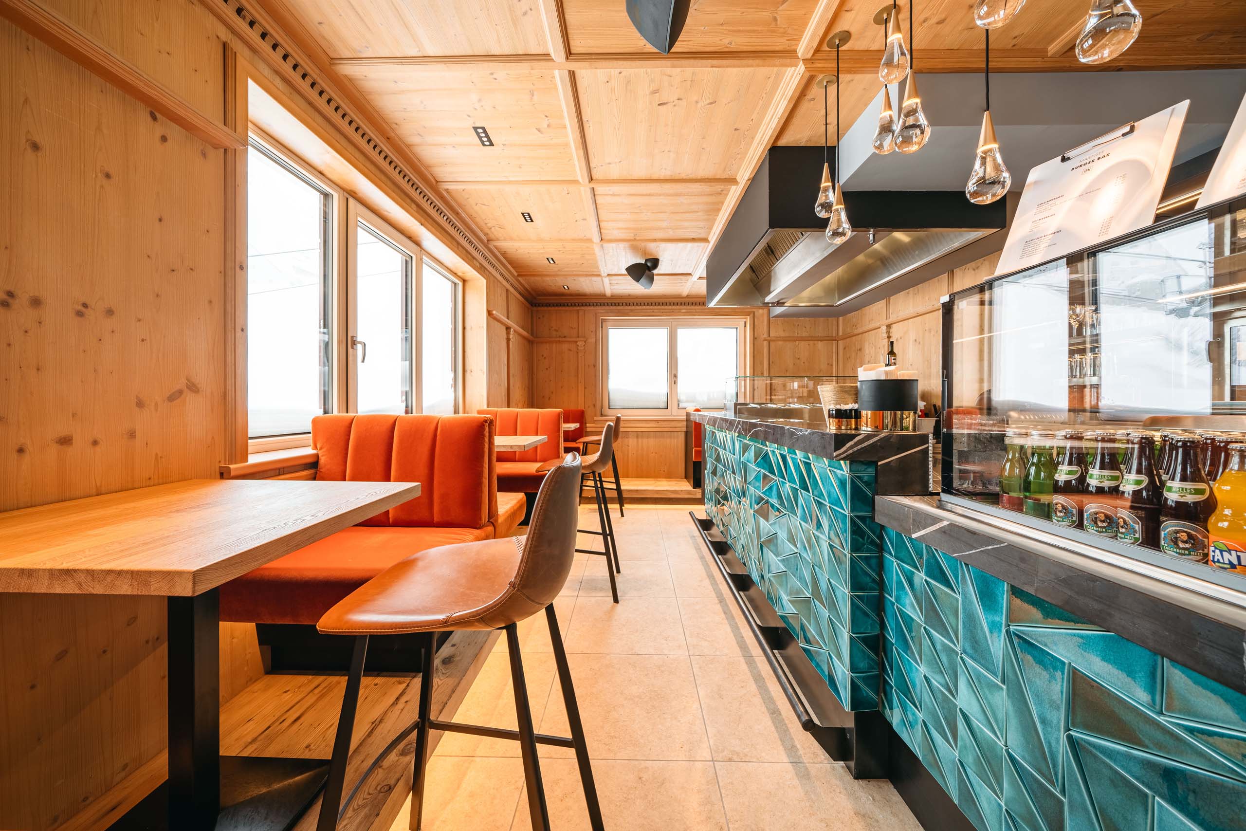 Burger im Skihotel in St. Anton am Arlberg Innenraum einer modernen Bar mit orangen Sitzbänken und blauer Fliesenbar
